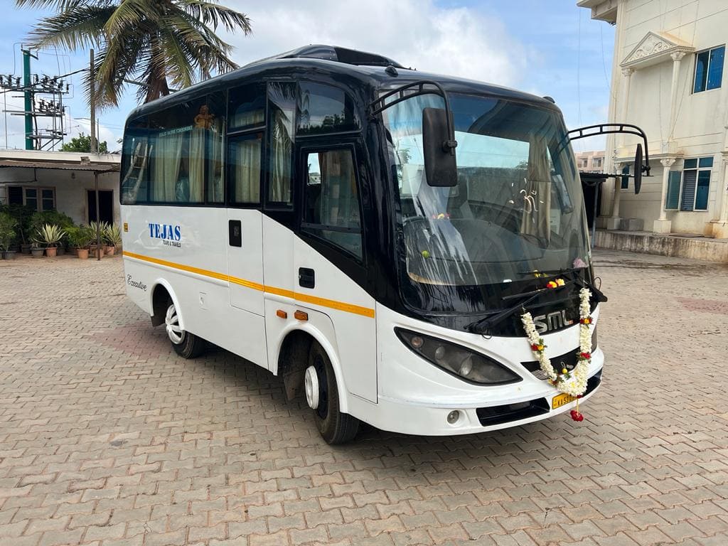 A decorated bus with "TEJAS" written on it is parked on a paved area, surrounded by palm trees and buildings.