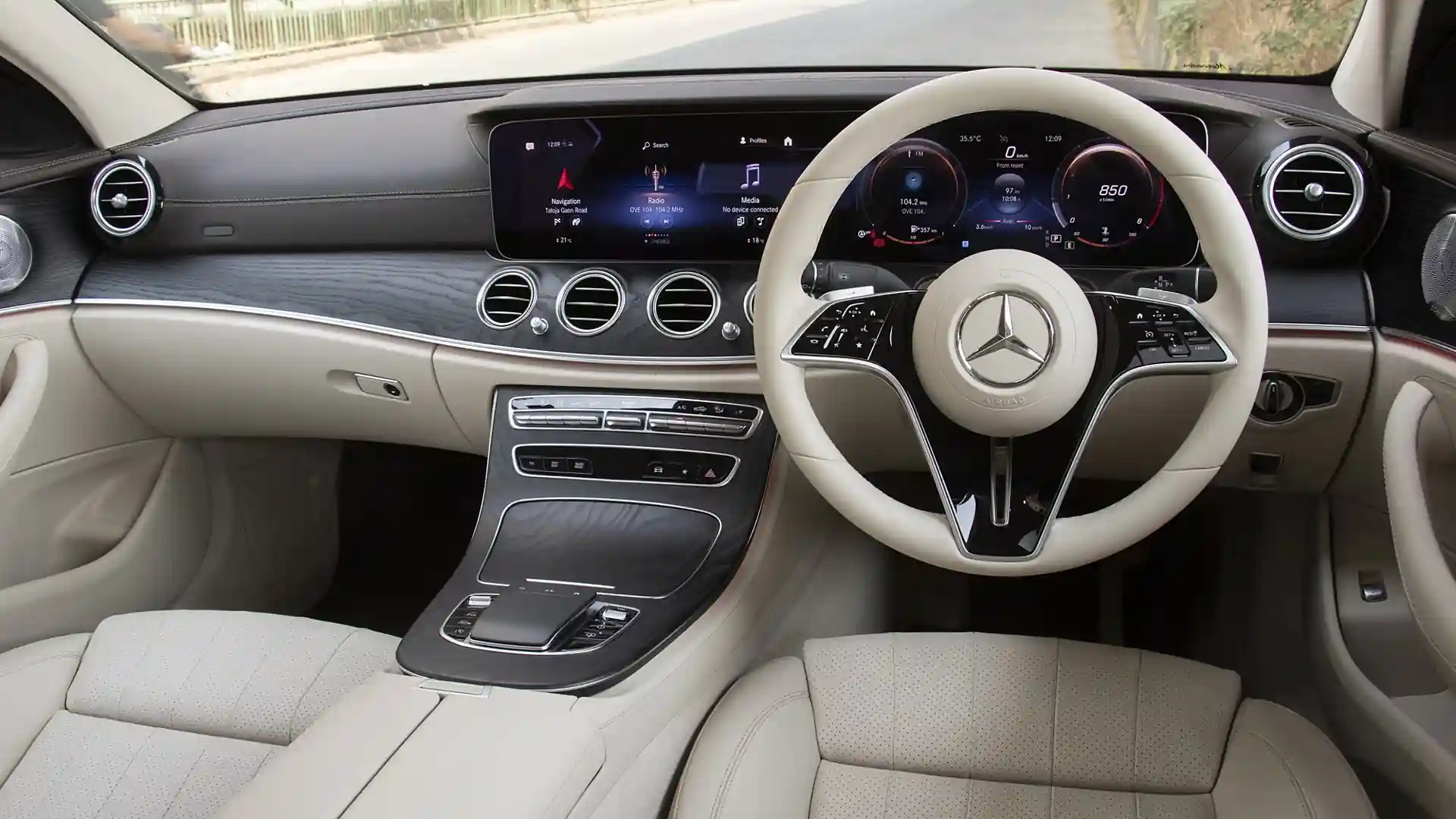 Luxurious car interior featuring a modern dashboard, touchscreen displays, and a sleek steering wheel in cream leather.