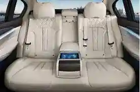 Luxurious beige leather back seats of a car, featuring a central console with a touchscreen display.