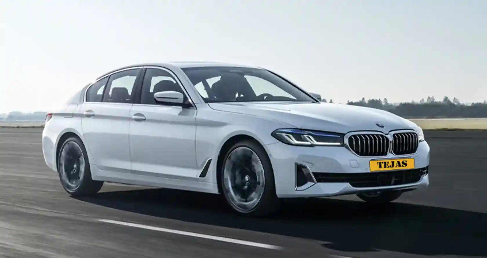 A sleek white BMW sedan drives on an asphalt road, showcasing its modern design and performance features.