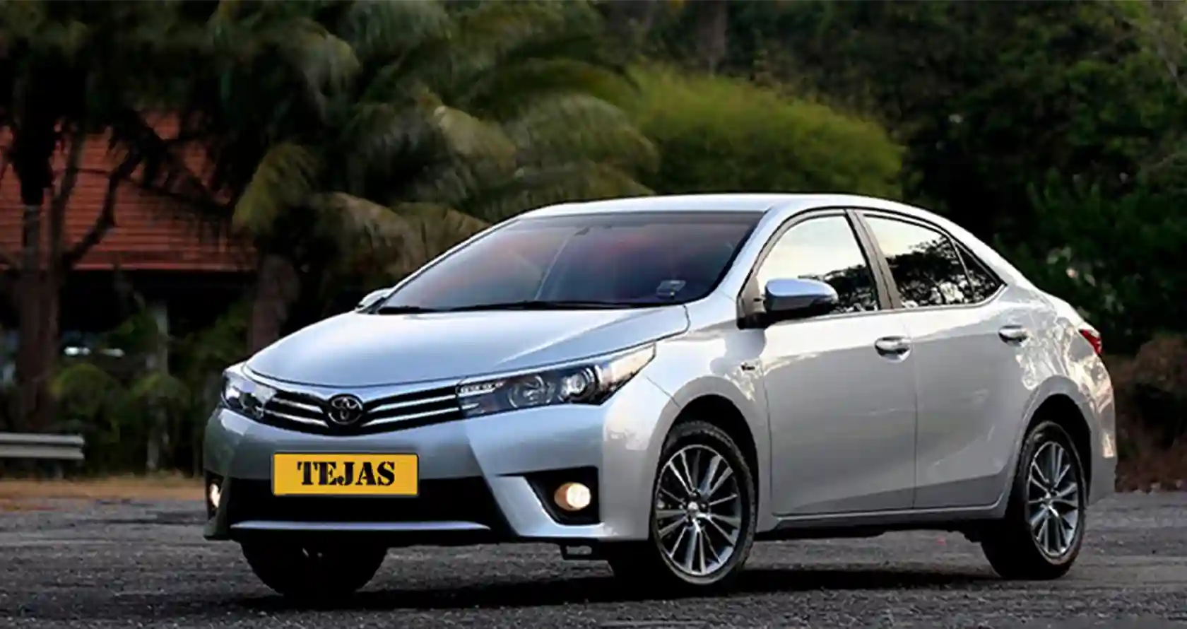 A silver Toyota sedan parked on a paved surface, surrounded by greenery and trees, with a visible license plate reading "TEJAS."