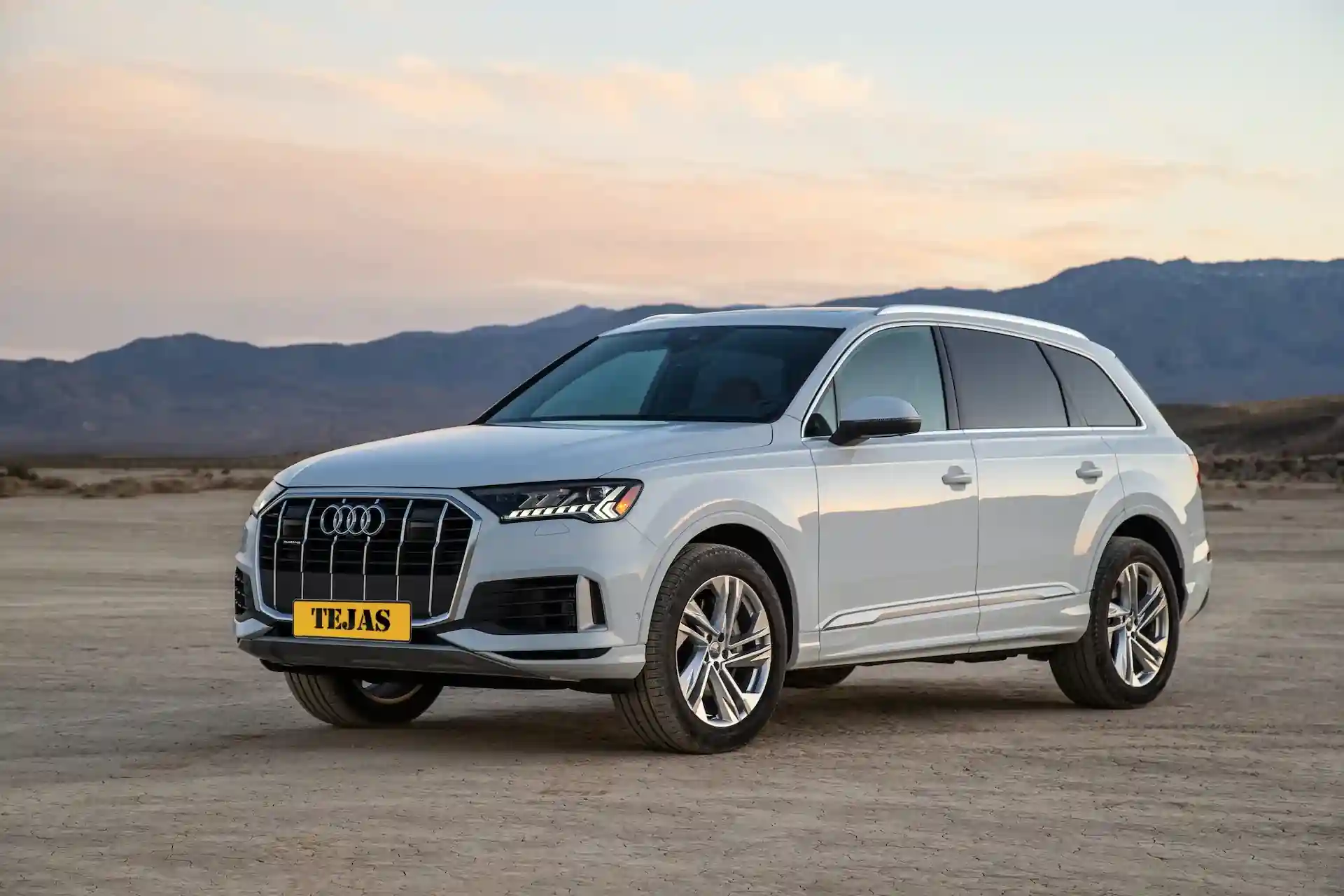 Silver Audi Q7 SUV parked in a desert landscape with mountains and a pastel sunset in the background.