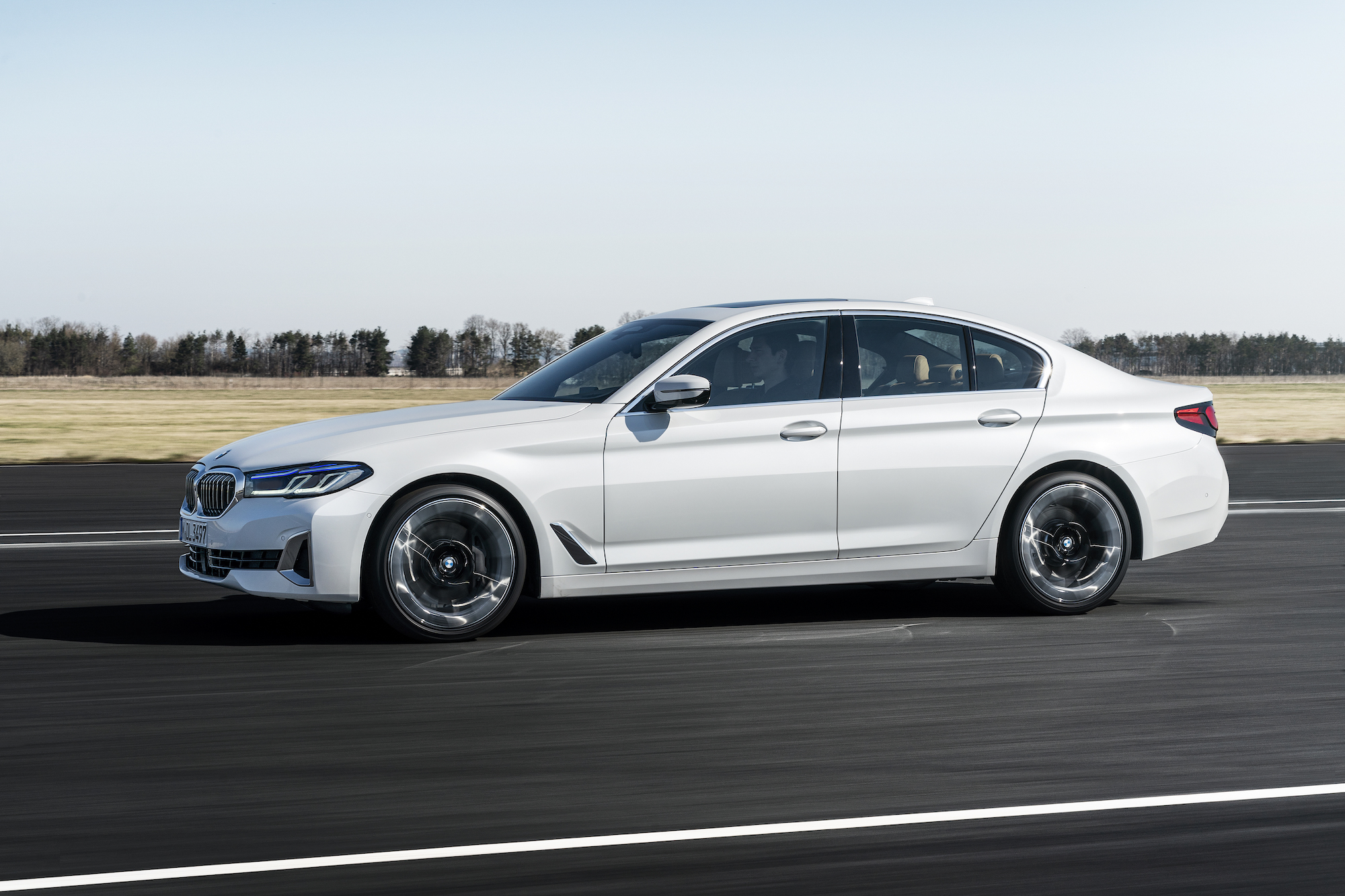 A sleek white BMW 5 Series sedan accelerates on an empty asphalt runway under a clear sky.