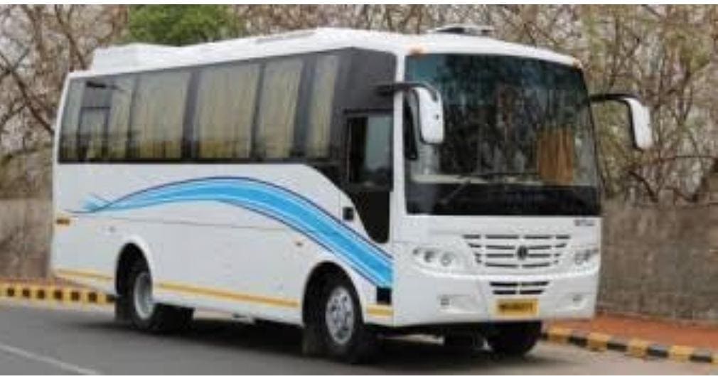 White bus with blue stripes parked on a roadside, surrounded by bare trees and a clear sky.