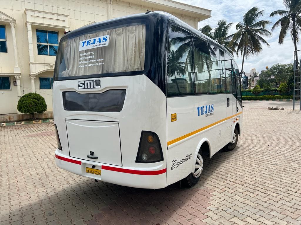 White travel bus parked on a cobblestone surface, with palm trees and a building in the background. "TEJAS" is written on the bus.
