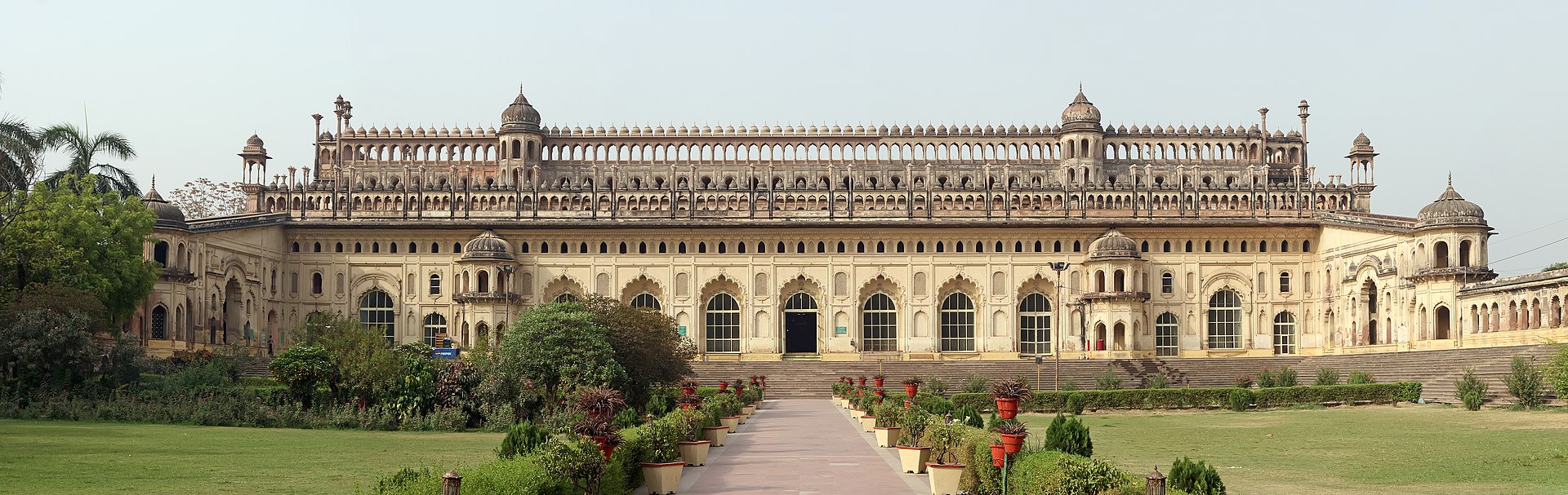 A grand historical building with multiple domes and arched windows, surrounded by a manicured garden and pathways.