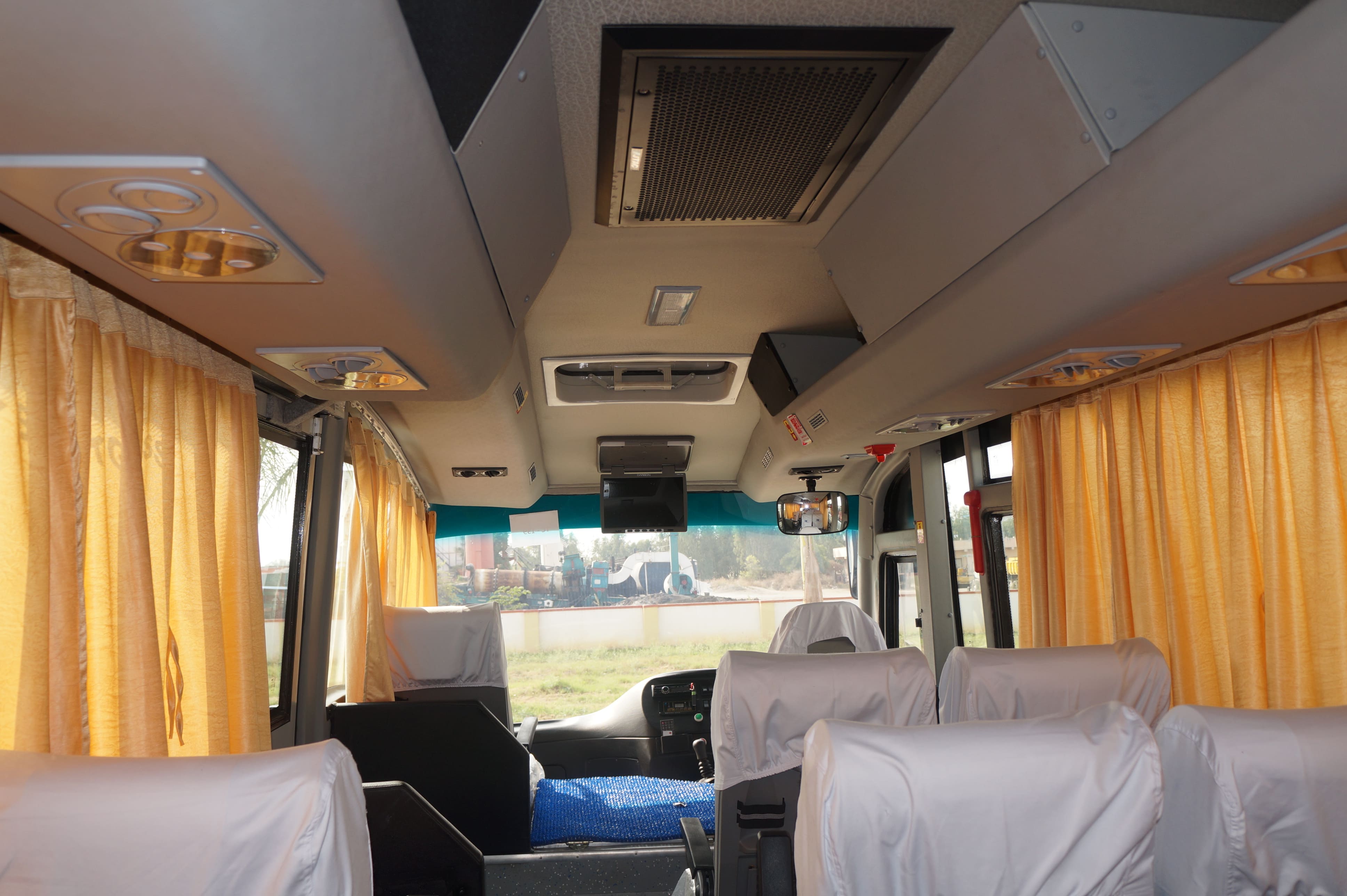 Interior of a bus featuring orange curtains, ceiling lights, and seats covered in white fabric.
