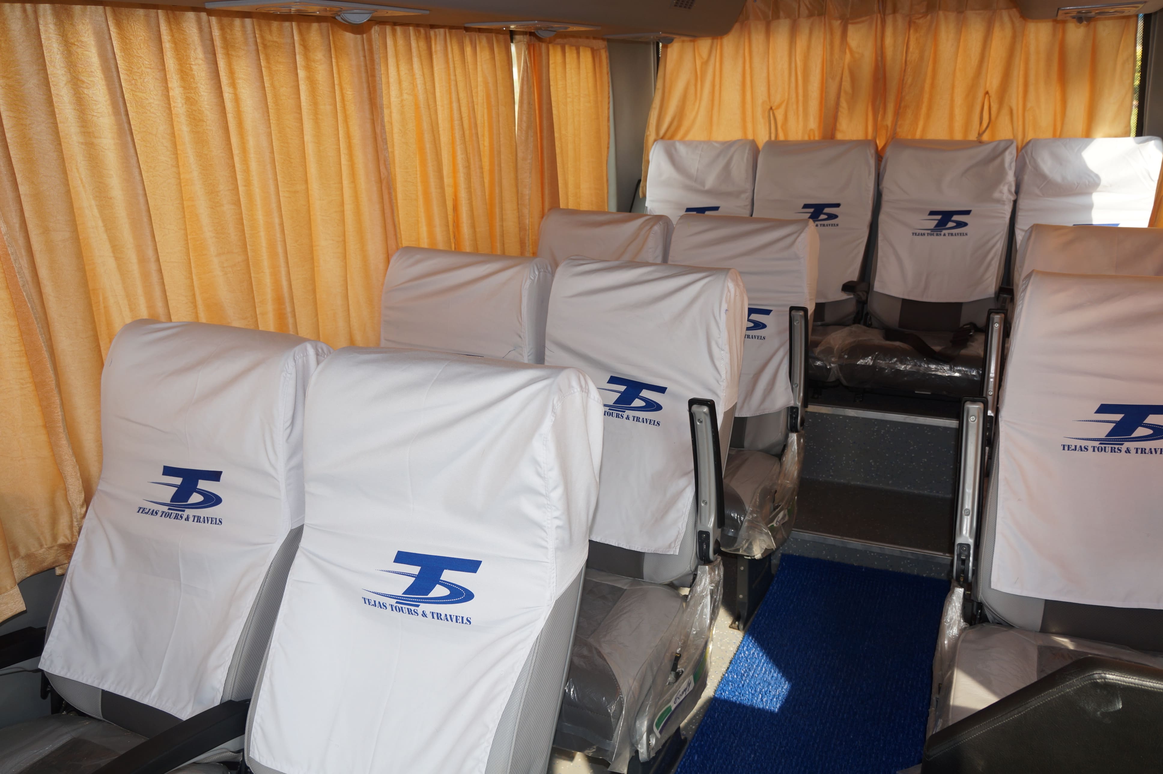 Interior of a travel bus with neatly covered seats and orange curtains, featuring a blue carpet aisle.