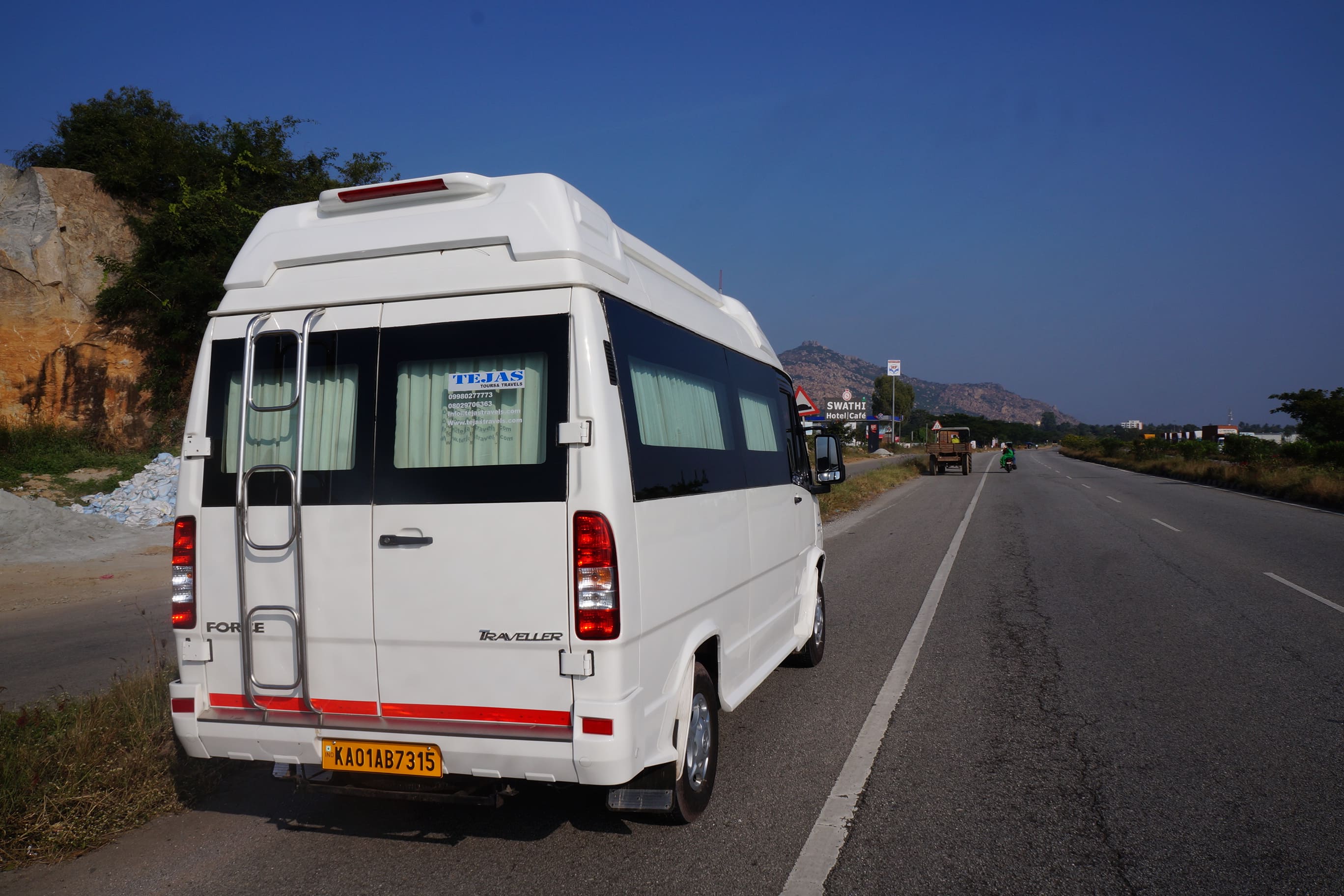 White van parked on the roadside, with a mountain backdrop and a road sign for a café visible ahead.