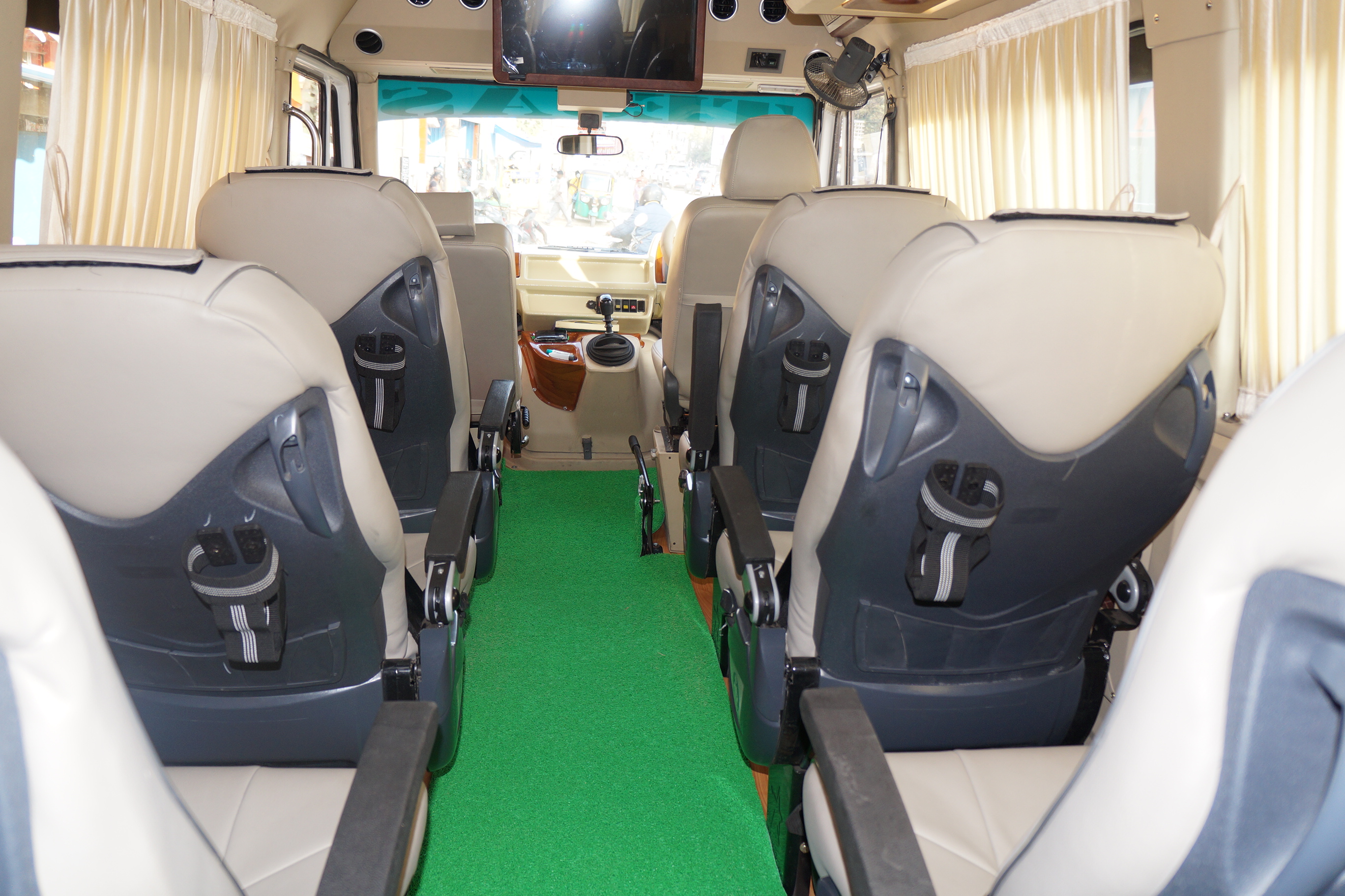 Spacious van interior featuring beige seats, green carpet, and a front dashboard with a television and controls.