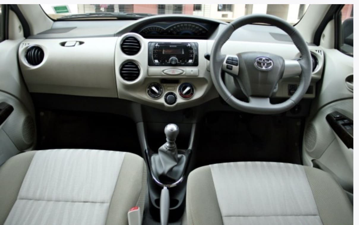 Interior view of a Toyota car featuring a steering wheel, gear shift, and dashboard controls, with fabric seats.