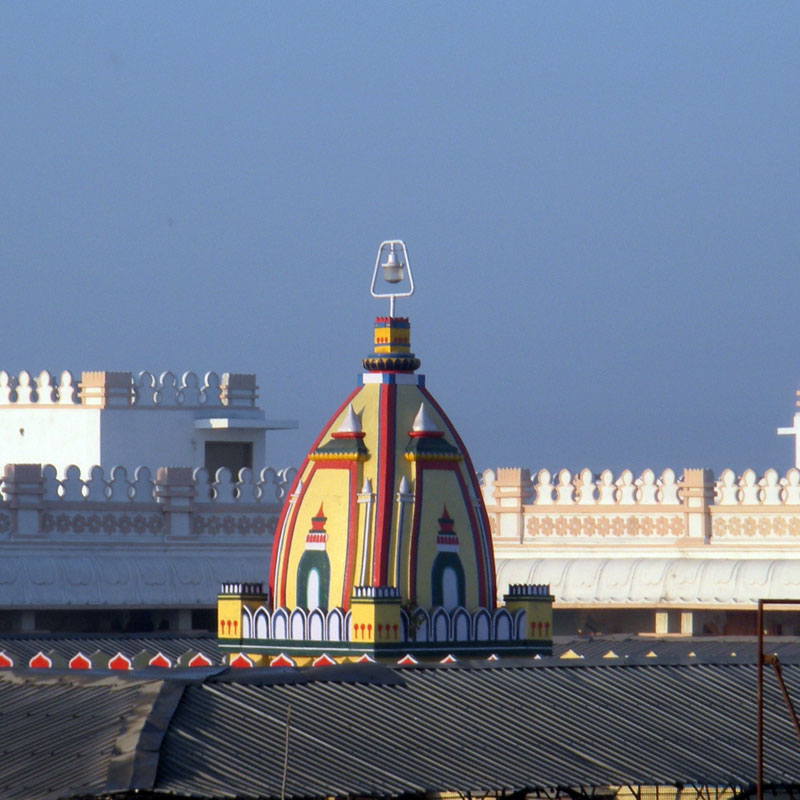 A colorful temple dome with intricate patterns and a lamp at the top, surrounded by white buildings against a blue sky.