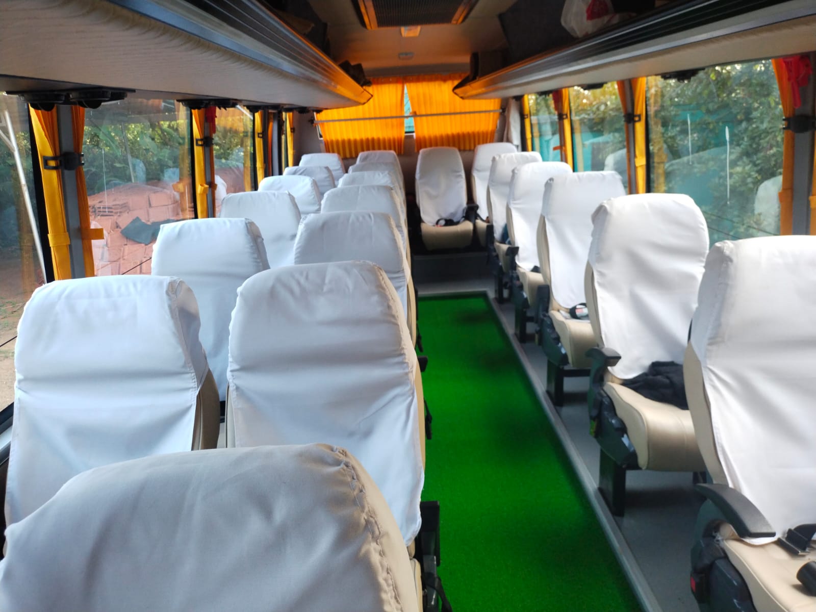 Empty bus interior with white-covered seats and a green aisle, illuminated by natural light through large windows.