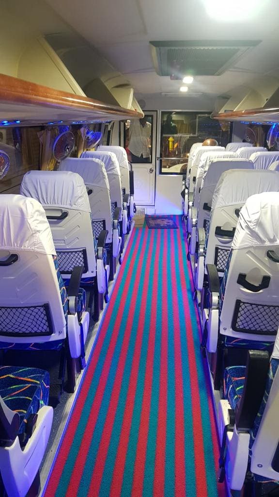 Interior of a bus with white seats, colorful striped carpet, and blue lighting, creating a modern and clean atmosphere.